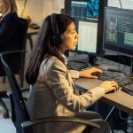 female agent of intelligence service sitting in front of computer monitors in office and processing personal data of criminals
