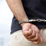 prison male criminal standing in handcuffs with hands behind back